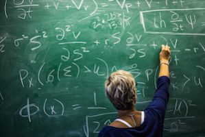 Woman works on complex math equation on chalkboard.